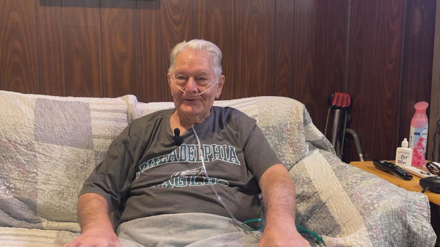 John Petroski sitting on his couch smiling, wearing an Eagles t-shirt 