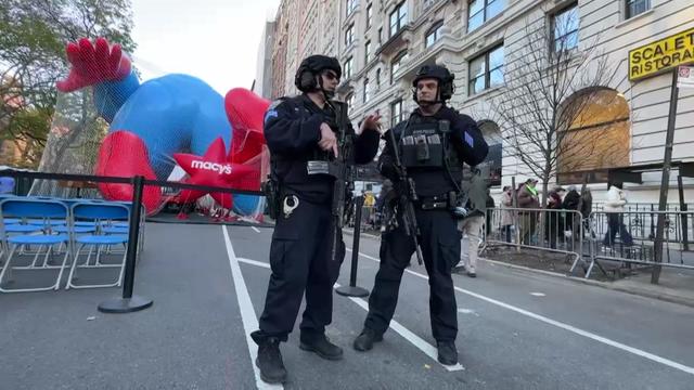 Two NYPD officers with guns stand at the end of the Macy's Thanksgiving Day Parade balloon inflation event. 