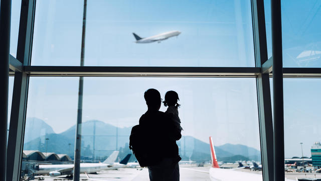 Silhouette of joyful young Asian father carrying cute little daughter looking at airplane through window at the airport while waiting for departure 