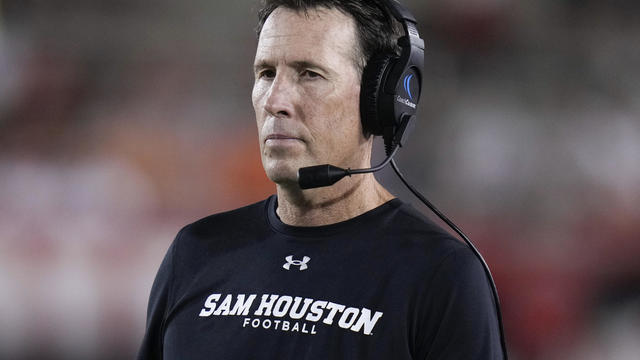 Sam Houston wears a headset and a Sam Houston football shirt on the sidelines of a football game 