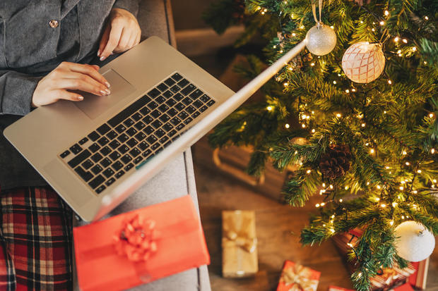 Close up of woman hands with, gifts, coffee cup and laptop. Online shopping at Christmas holidays. Freelance girl woking from home office. Female typing at notebook computer. Christmas moments. 