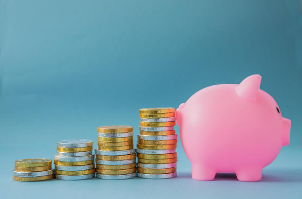 Children savings concept with stacks of gold and silver coins in an upward growth profit graph leading towards a pink, kids Piggy bank 