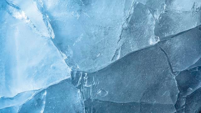 Full frame, frozen water surface in a river with cracks and broken ice crystals of turquoise blue color. 