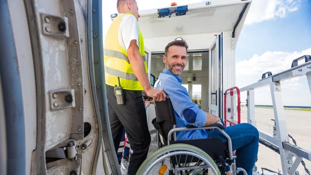 Service man helping disabled passenger to enter on board at airport 