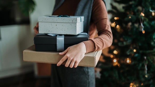 Cropped shot of young Asian woman holding stack of wrapped Christmas presents in hands, standing next to the illuminated and decorated Christmas tree at home. Christmas lifestyle theme. Celebrating Christmas. Holiday and festive vibes 