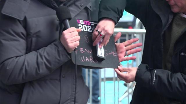 An individual holds a small slate with several words written on it as another individual erases it. 