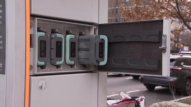 An e-bike battery charging station. The door to one section is open to show four batteries plugged in to charge. 