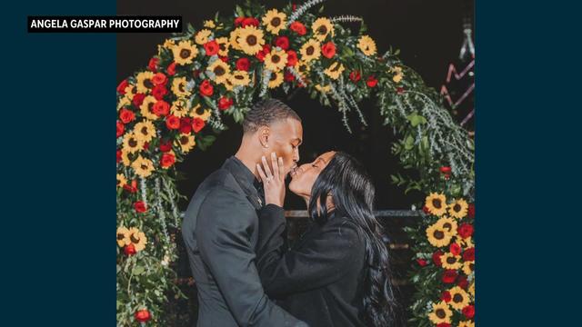 DeVonta Smith and Mya Danielle kiss in front of a floral arch and the Philadelphia skyline 