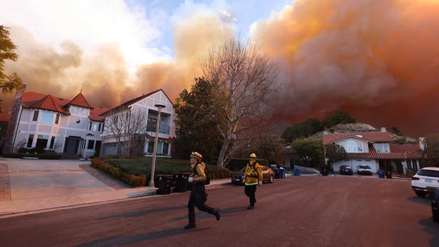 Firefighters run on a residential street as a brush fire burns in Pacific Palisades, California 