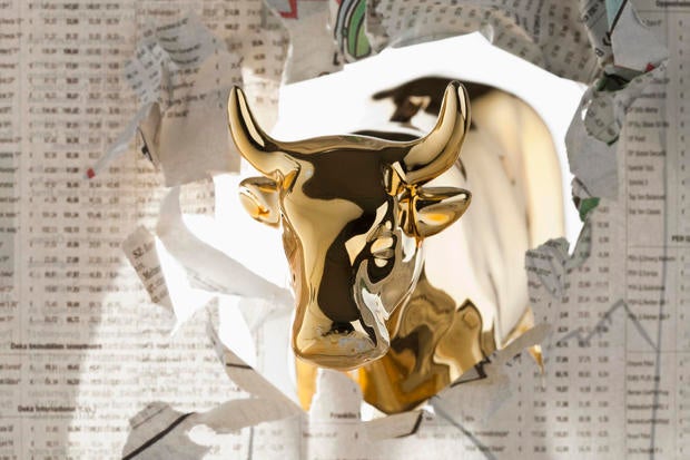 A golden bull breaking through the finance section of a newspaper