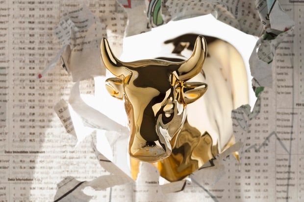 A golden bull breaking through the finance section of a newspaper