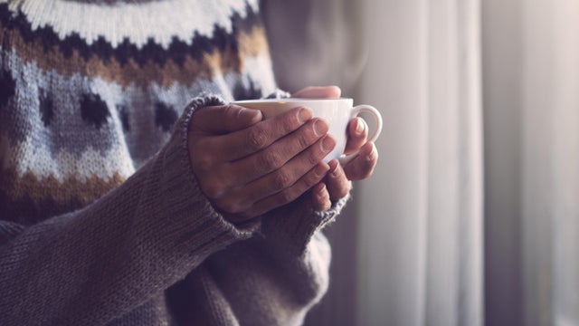 Woman in knitted sweater hands holding cup of warm coffee