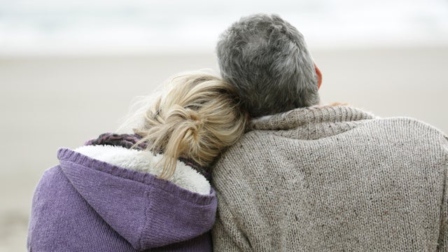 Couple sat on beach in winter looking out to sea 