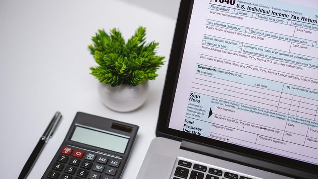 Tax Form on Laptop Screen on Work Desk with Pen and Calculator 
