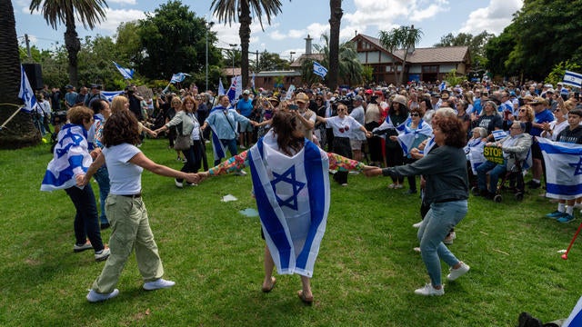 Protesters hold signs and wave Israeli flags as others dance 