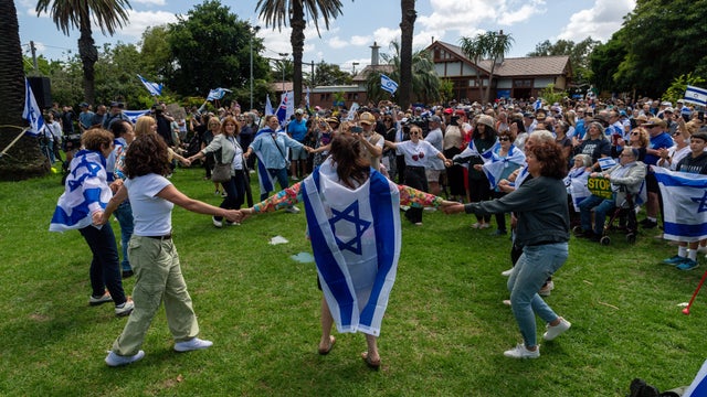 Protesters hold signs and wave Israeli flags as others dance