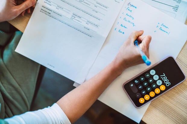 Overhead view of young Asian women managing home finance using smartphone. She is working with household utility bill and  calculating expenses at home.