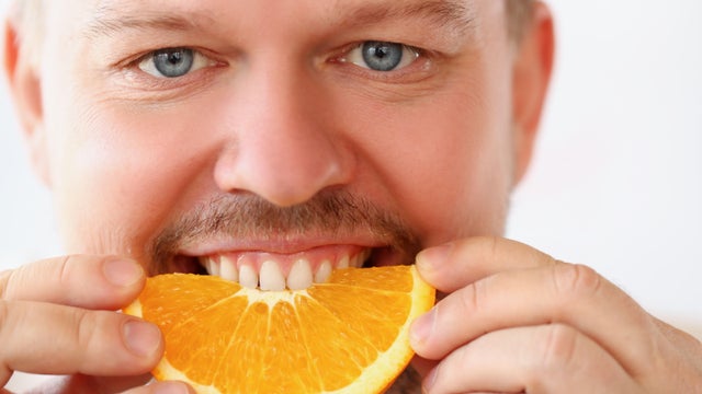 Man bite chopped slice of orange for breakfast in kitchen, healthy eating, strict diet