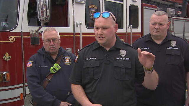 Three firefighters speak to a reporter in front of a firetruck 