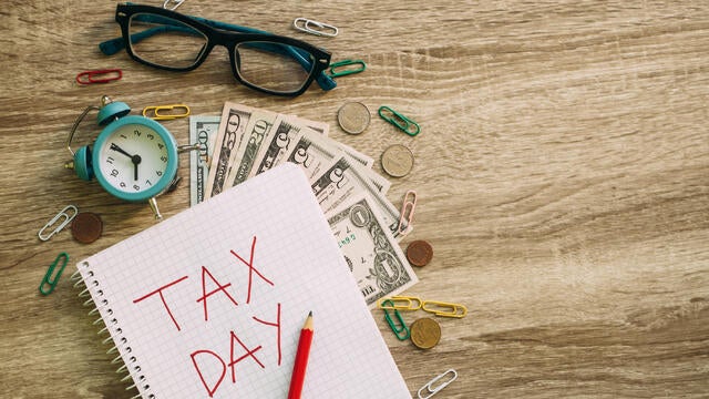 Tax day written in red into the notebook, office table background 