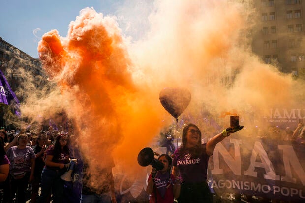 Women hold up cans releasing red-colored smoke outside La Moneda presidential palace during a march marking International Women's Day, in Santiago, Chile