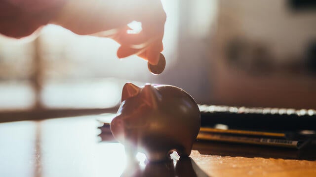 Hand and a piggy bank and coin on a table in backlight. 