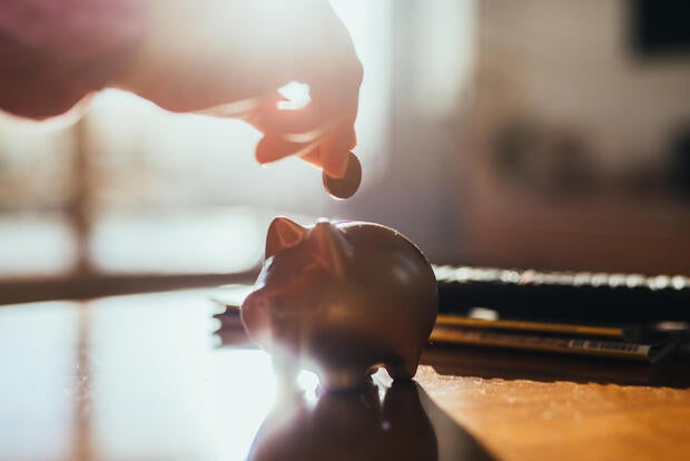 Hand and a piggy bank and coin on a table in backlight. 