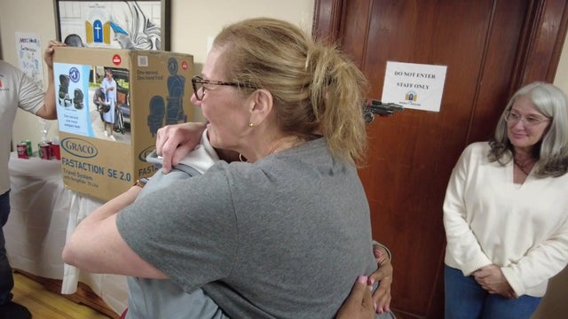 Two women hug. A box for a car seat/stroller can be seen on a table in the background. 