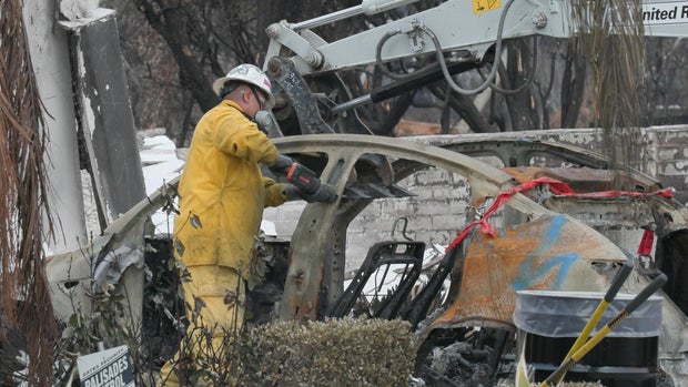 Workers handling the charred remains of an electric vehicle after California wildfires 