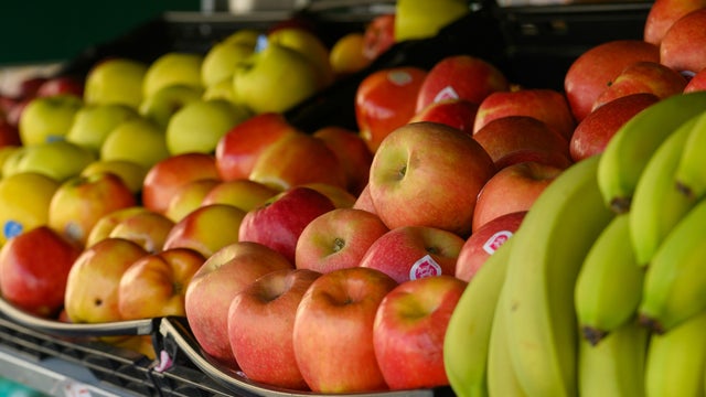 Cropped shot of young Asian woman choosing fresh organic fruits in supermarket. She is picking a red apple along the produce aisle. Routine grocery shopping. Healthy living and eating lifestyle 