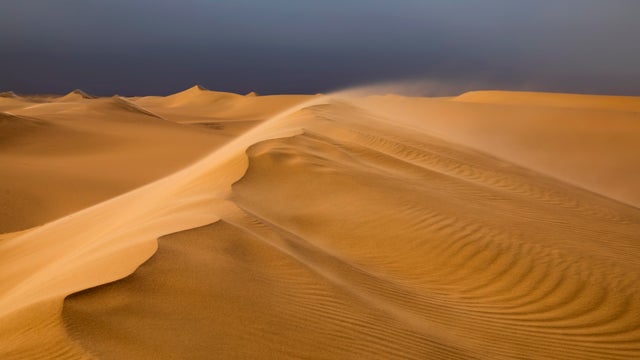 Strong wind at sunset over the sand dunes in the desert. Sandstorm in the Sahara Desert