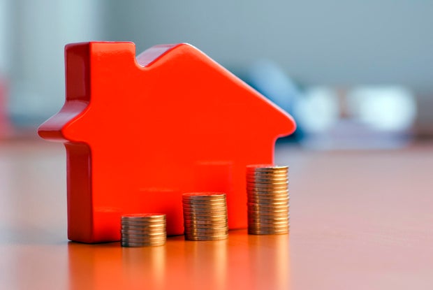 Red 3D house model next to growing stacks of coins 