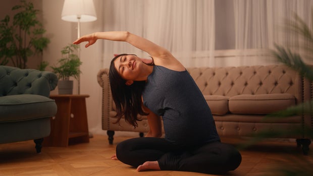 Pregnant woman sitting on ground and doing breathing and stretching exercises in living room at home