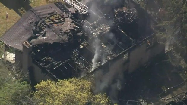 Overhead photo of a home severely damaged by a fire, part of the roof is caved in, the home is charred black 