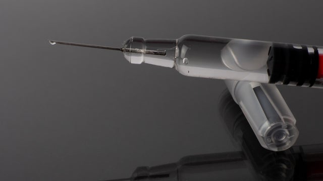 Syringe with fine needle with a drop of medication reflected on a gray background with mirror effect 