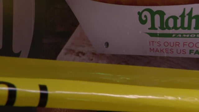 A bullet hole can be seen in the side of a food cart behind crime scene tape. 