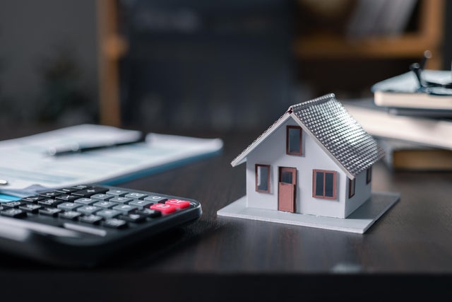 Model house, paperwork and cash money on a desktop: real estate, home loan and investments concept. Small houses with modern design calculator and pen on office background for home loans concept