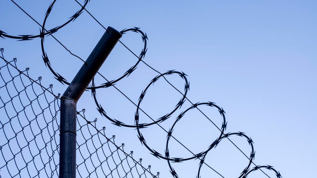 Close-up of metal fence with barbed wire over a blue sky. 
