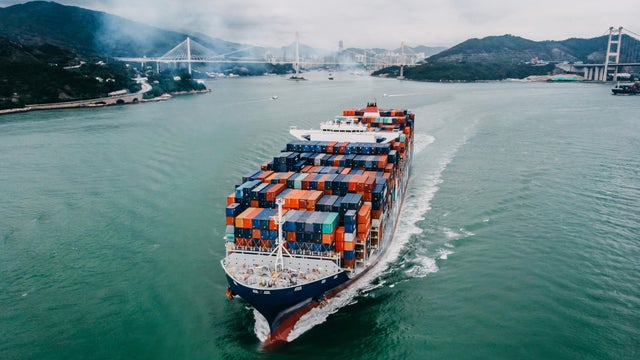 Aerial view of container ship transporting goods sailing across ocean leaving the port 