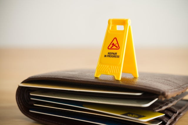 Close up yellow warning sign Repair in progress on wallet with many credit card white wall background.