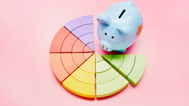 High angle view of a piggy bank and colorful pie chart on pink background 
