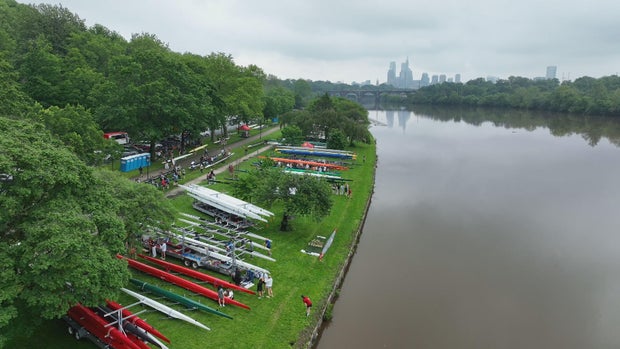 Drone shots of boats lined up on the banks of the Schuylkill River ahead of the Regatta, it's cloudy but the Philadelphia skyline is visible in the distance 