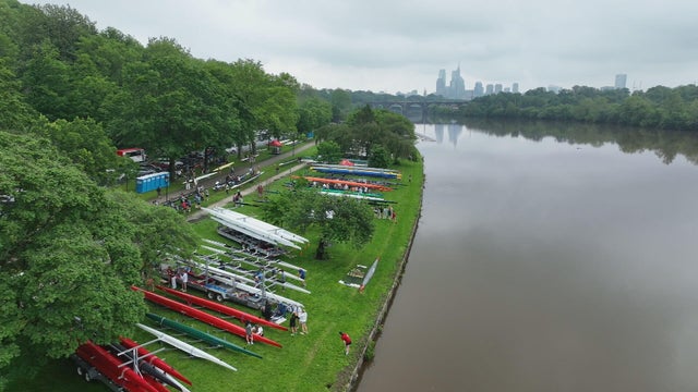 Drone shots of boats lined up on the banks of the Schuylkill River ahead of the Regatta, it's cloudy but the Philadelphia skyline is visible in the distance 