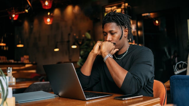 sad black man sitting at table with laptop in cafe 
