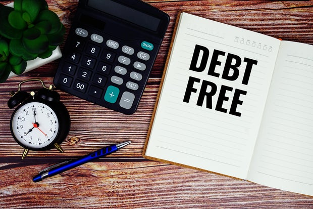 Debt Free text written on paper torn with calculaton and alarm clock top view on wooden background 