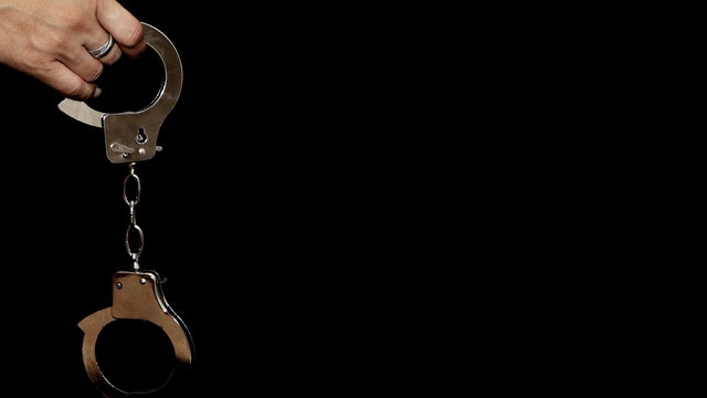 Female hand holding handcuffs against black background 