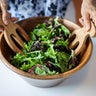 Female hands mixing various vegetable in wooden salad bowl. 