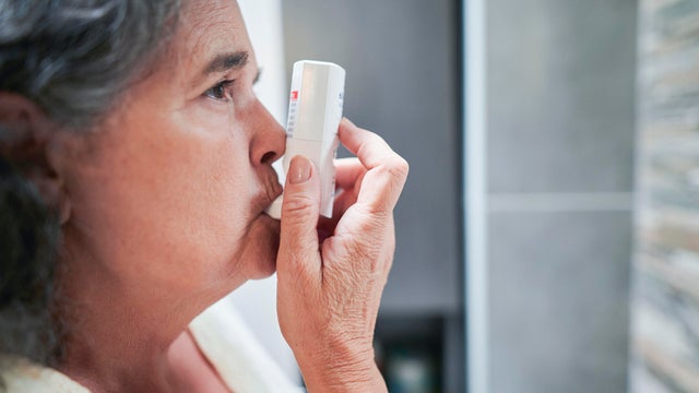 Woman using inhaler in bathroom 
