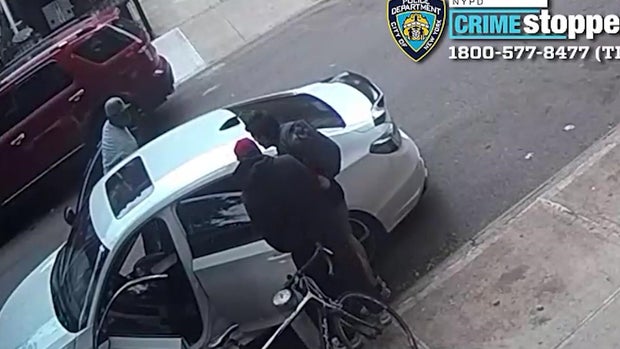 A suspect tries to pull a man into the back seat of a sedan while a second suspect watches. 