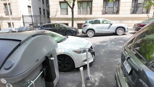 A large Empire trash bin along a curb in New York City. A vehicle is parked in the street next to it. 